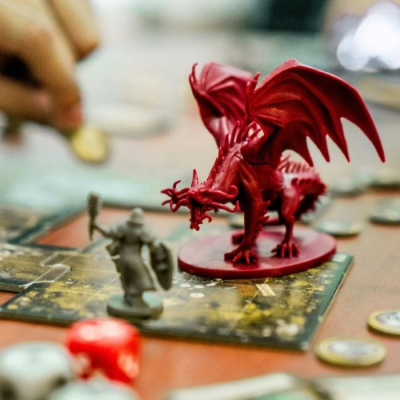 A dragon figurine standing on a dungeon tile with dice and coins nearby