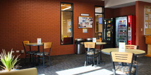 Little cafe room in the public library with a few small tables with a couple of chairs. Vending machines are in the background.