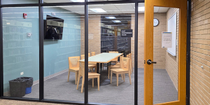 Room in the library with a long table, chairs around the table, tv on the wall, and glasses windows and a glass door