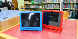 two iPads in a blue and red iPad case sitting on a table with bookcases in the background