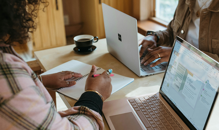 Two people sitting at a table with open laptops and notebooks