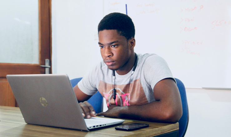 Male teen sitting in a study room and looking at his laptop screen